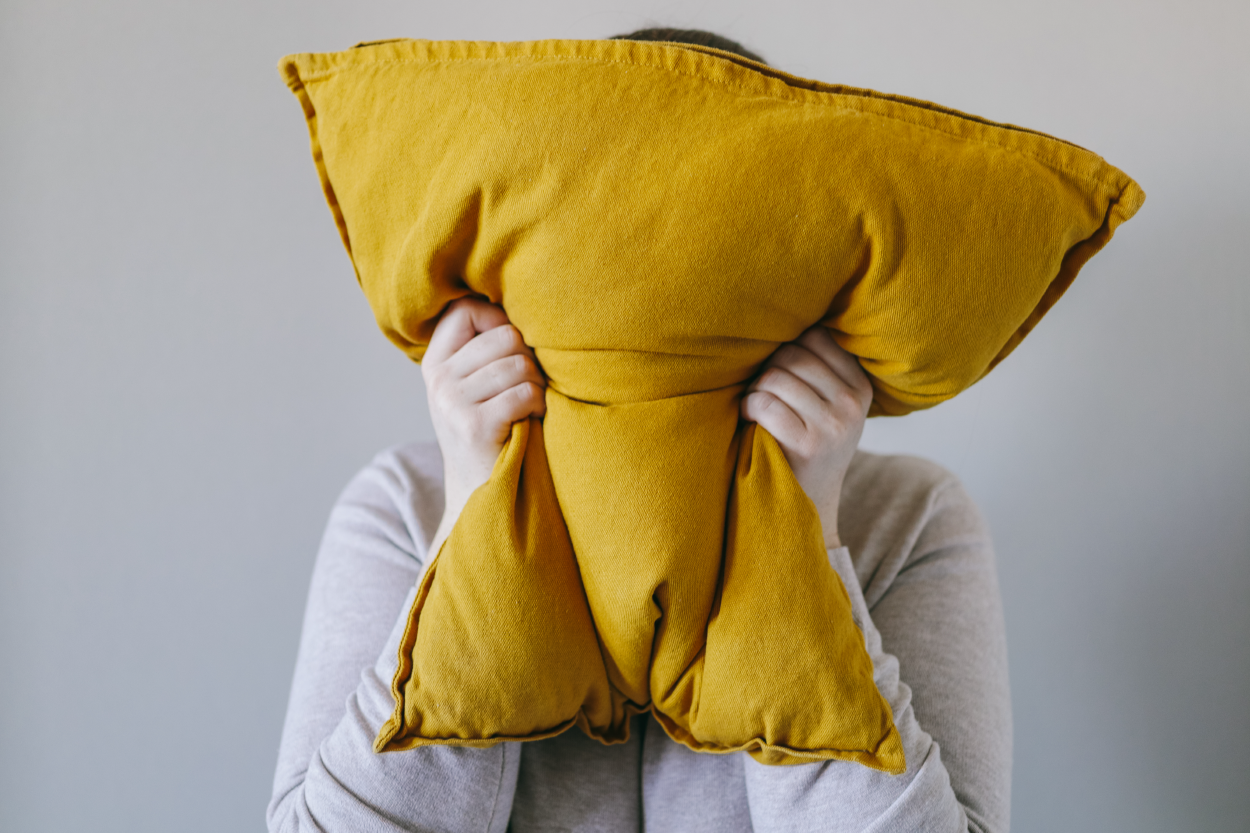 a person covering their face with a yellow pillow; they are squeezing it hard like they are yelling into the pillow