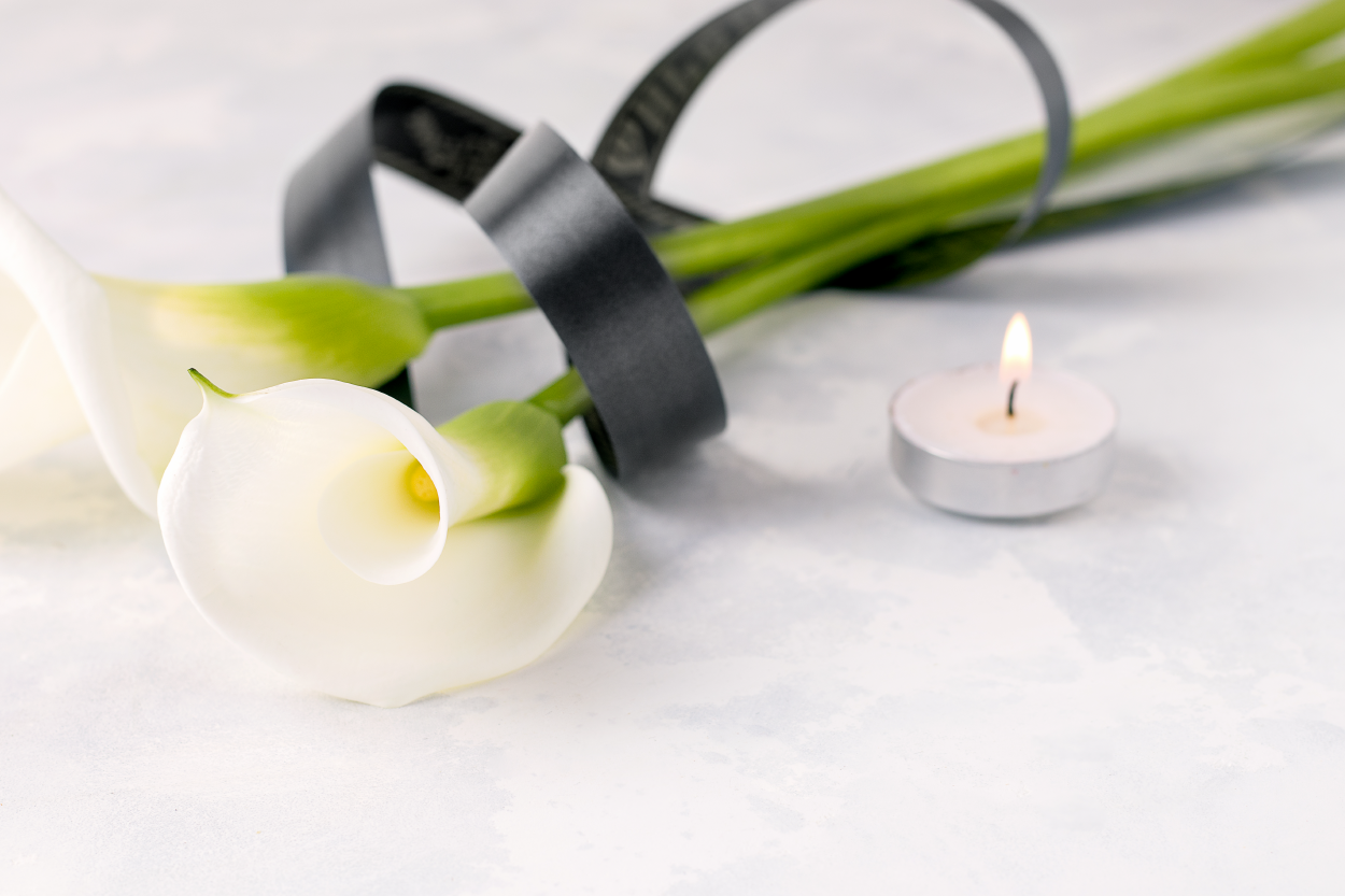 two white flowers with black ribbon lying beside a lit tea candle