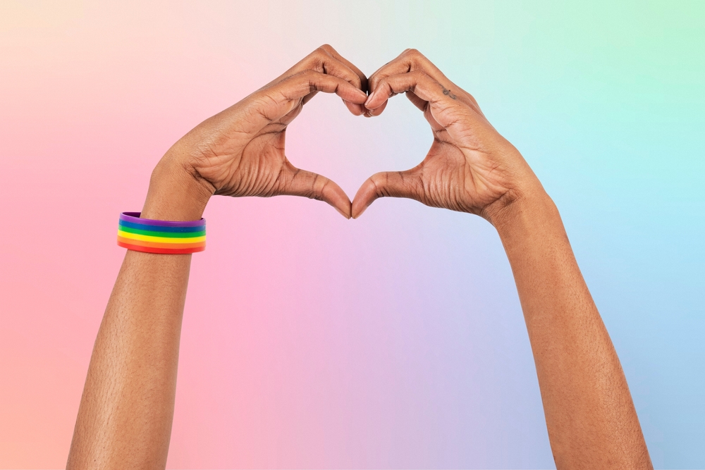two hands form a heart; one has a rainbow bracelet on the wrist