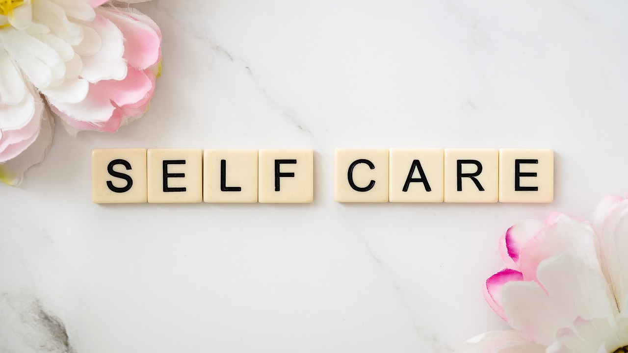 tiles spelling self-care on table with two pink and white flowers