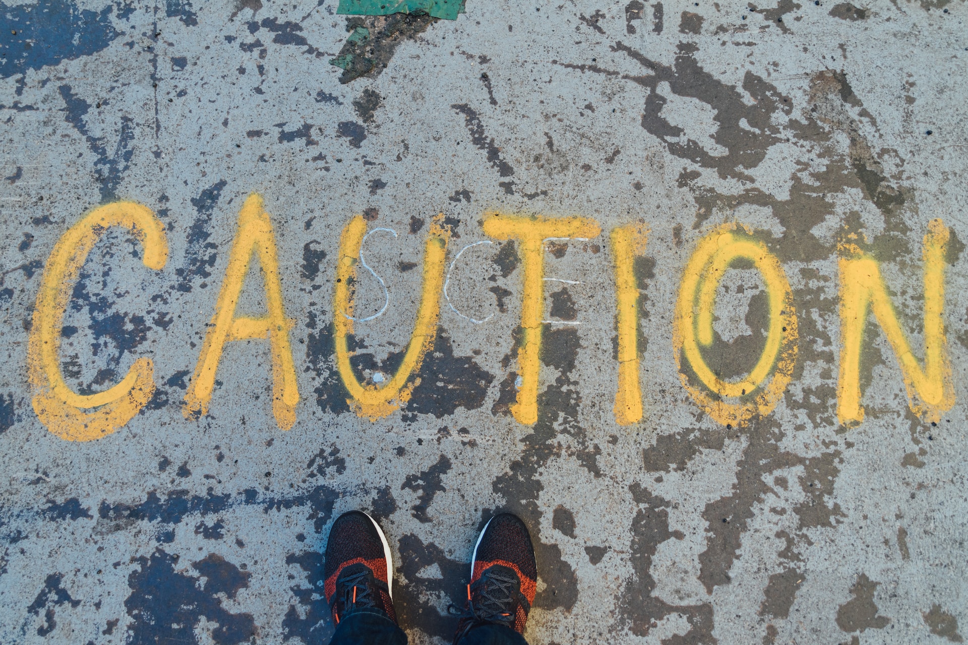 A person's feet in sneakers standing on a street before the word caution written in yellow chalk
