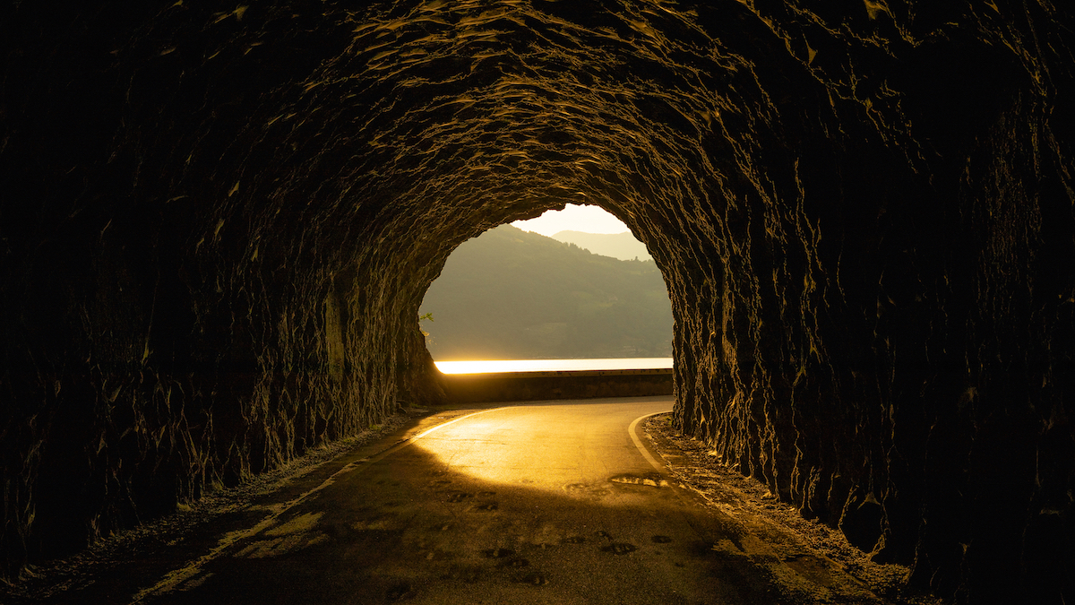 A street in a rocky tunnel with an amazing sunset coming through at the end