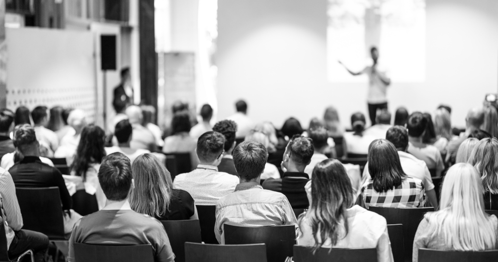 black-and-white image of a speaker giving a talk in front of a large audience